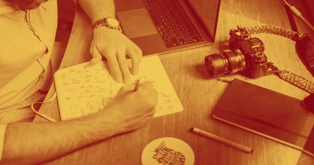 A man writes on a notebook trying to find the perfect font for his brand style guide. This is one of the many aspects of a brand style guide and is a crucial component of a marketing plan. 