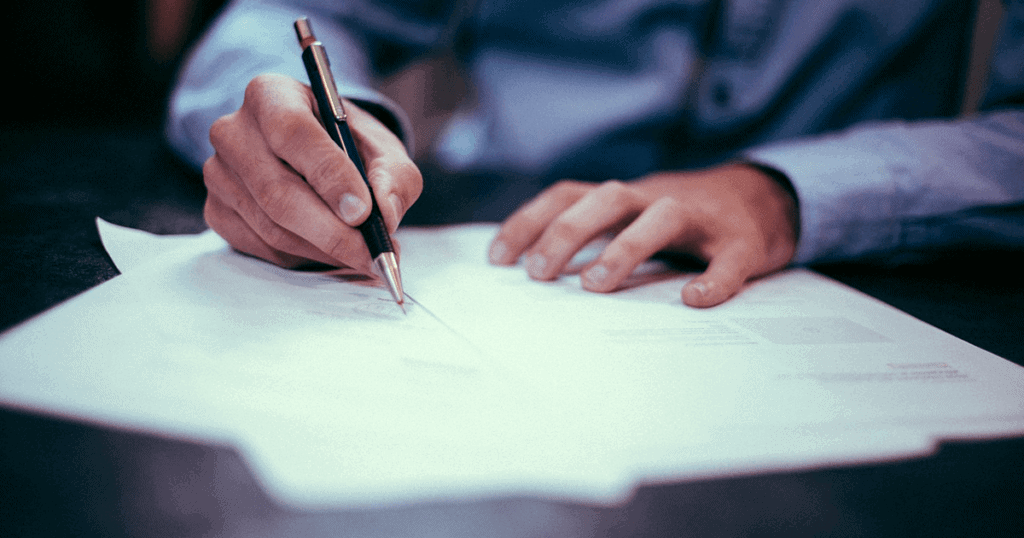 A business person writing notes on paper with a pen. Writing a press release like the one pictured doesn't have to be tough or mind-bending — learn more.