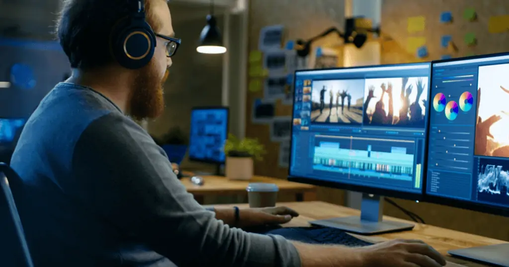 A man with a beard and glasses sits at a dual-monitor workstation, editing videos. IGTV, a popular video app, is an effective marketing tool. Tips are provided in this post.