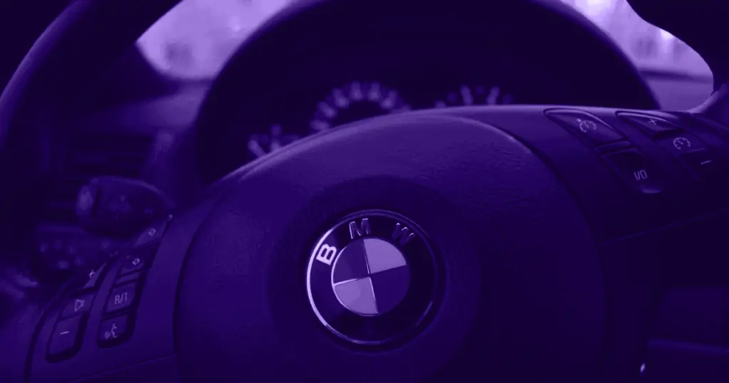 A modern dashboard and car steering wheel baring the BMW logo is pictured, shaded in purple. BMW is a great example of why branding beats marketing.