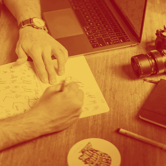 A man writes on a notebook trying to find the perfect font for his brand style guide. This is one of the many aspects of a brand style guide and is a crucial component of a marketing plan.