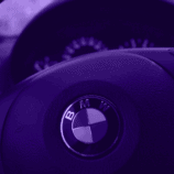 A modern dashboard and car steering wheel baring the BMW logo is pictured, shaded in purple. BMW is a great example of why branding beats marketing.