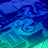 Becoming Branding Beasts—a number of items, including a pennant, a folded T-shirt, and a book, are laid out on a wooden table. The photo has a dark blue to aqua gradient.