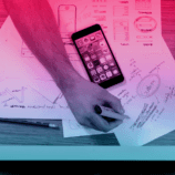An overhead view of a person's desk. Their hands are visible, holding a highlighter. Next to a number of documents is a cell phone. The person may be working on an answer to the question, "What is digital marketing?"